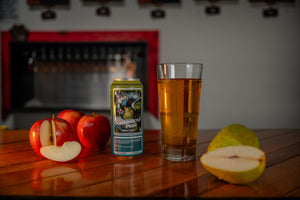 Glass of pear cider and the cider can on a wooden table with apples and pears.